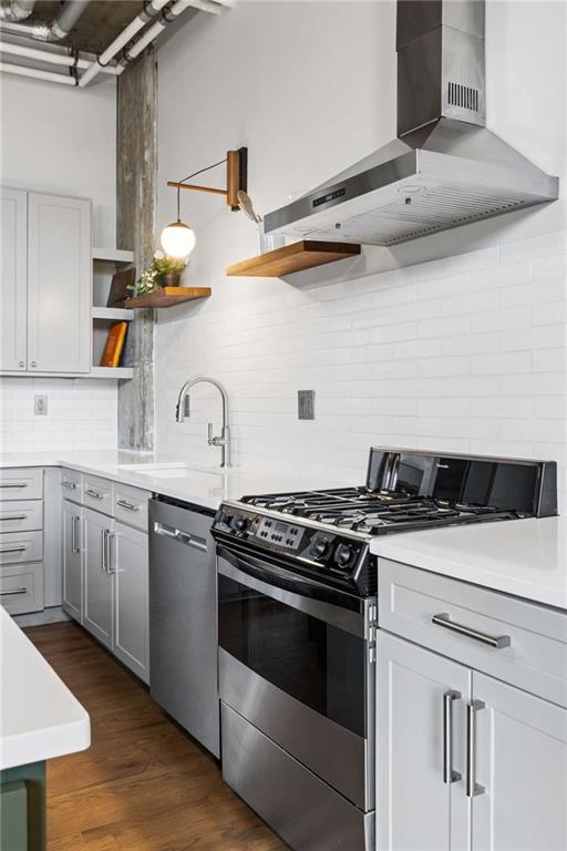 Modern white kitchen with stainless steel gas range, subway tile, and warm wood flooring.