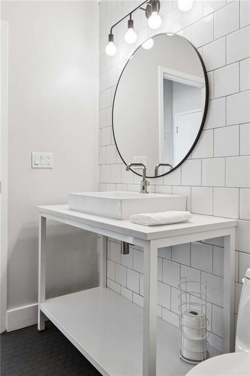 Bathroom vanity with a vessel sink, round mirror, white subway tile, and black hexagonal floor.