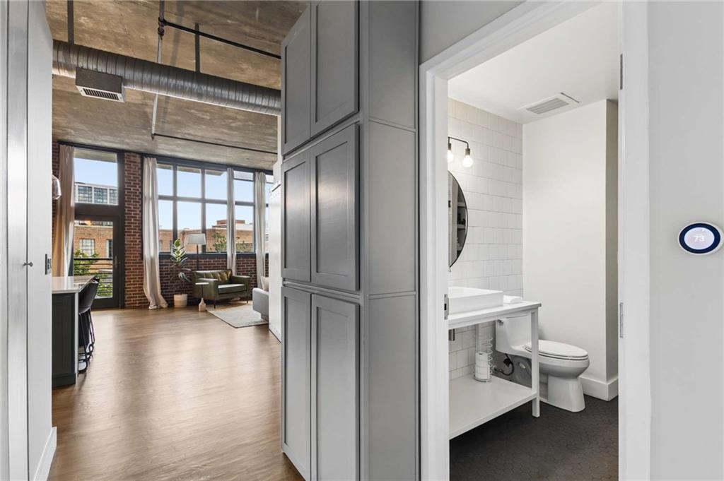 Condo interior with a tiled bathroom opening onto a bright living area with tall windows and exposed concrete ceilings.