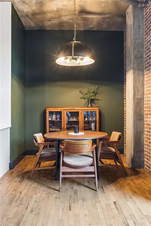 Dining area with a round wooden table, glass-front cabinet, dark green walls, and exposed brick.
