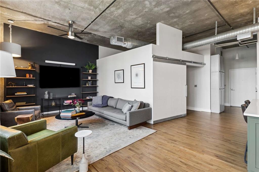Living room with a gray sofa, dark media wall, exposed concrete ceiling, and hardwood floors.