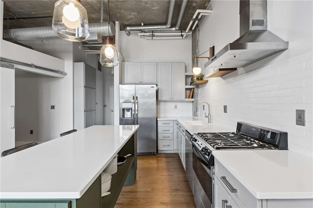 Modern kitchen with a long white island, stainless steel appliances, and exposed ceiling ductwork.