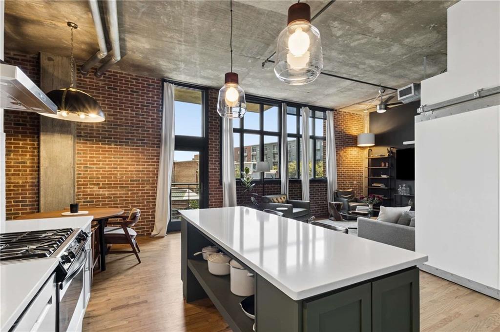 Loft kitchen with a large white island, exposed brick walls, and tall windows overlooking neighboring buildings.