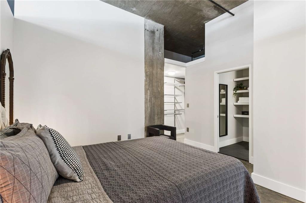 Bedroom with a gray bed, exposed concrete column, and open closet.