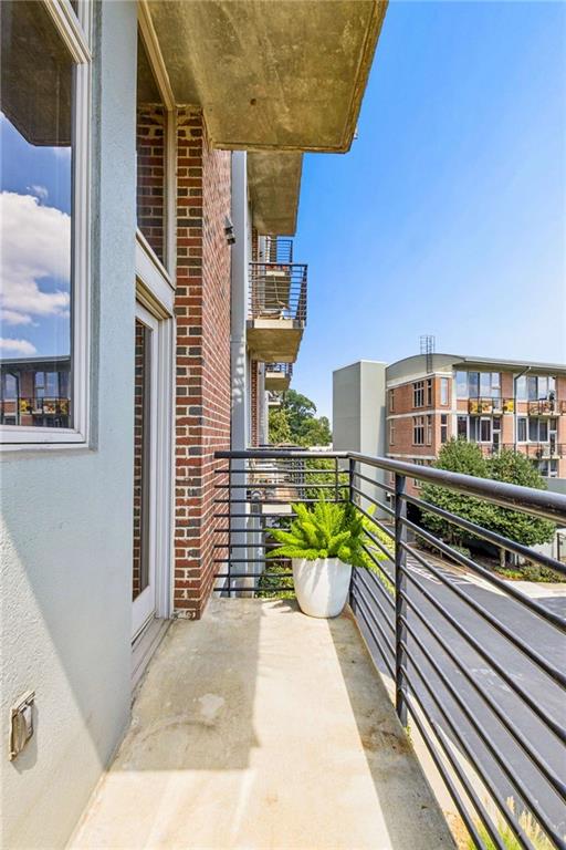 Condominium balcony with black railings, a potted fern, and neighboring apartment buildings.