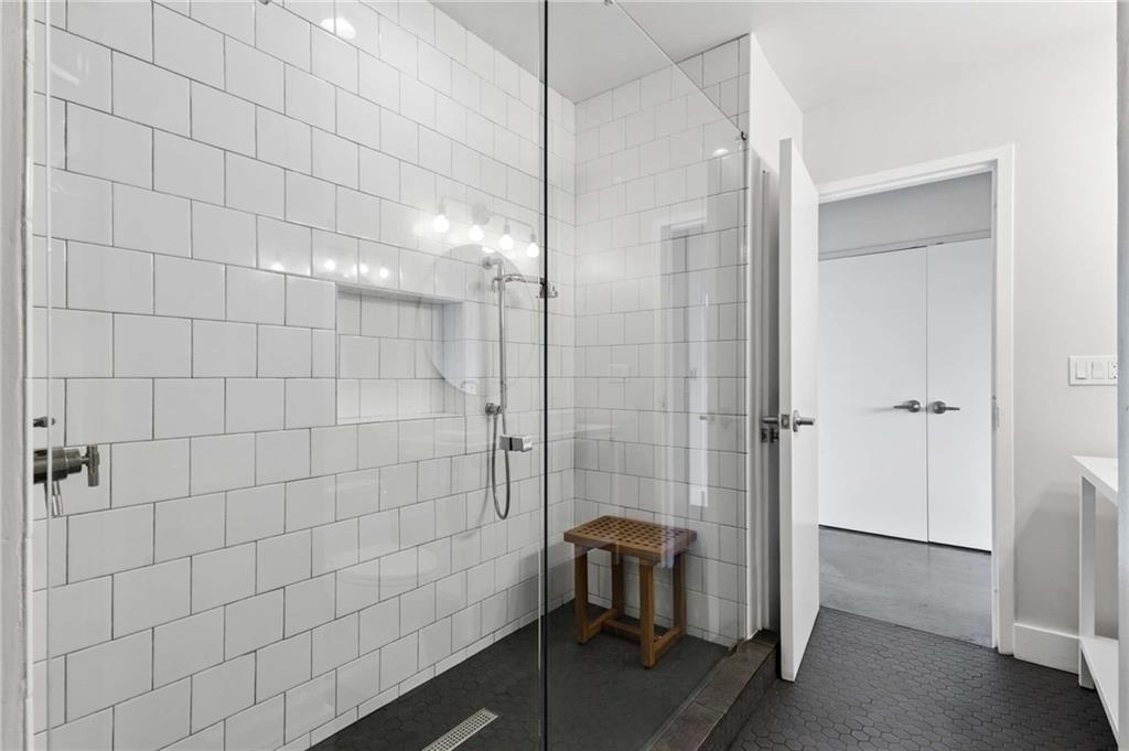 Bathroom with a glass walk-in shower, white subway tile, dark hexagonal floor, and wooden stool.