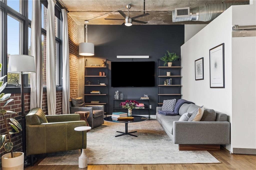 Living room with tall windows, exposed brick, a dark media wall, and gray sofa.