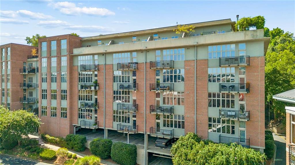Condominium building with red brick facade, rows of balconies, and landscaped grounds.