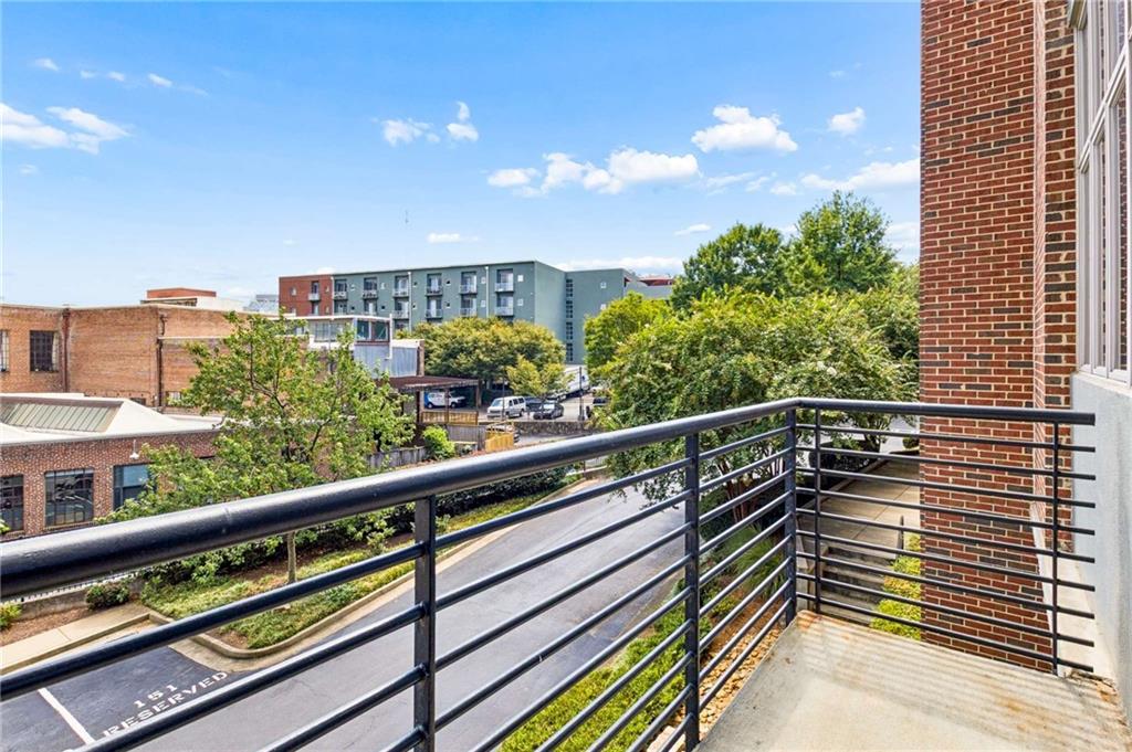 Condominium balcony overlooking a tree-lined street and nearby buildings.
