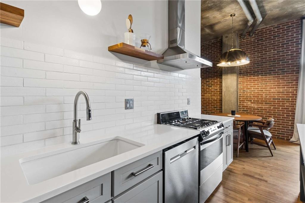 Modern kitchen with a deep sink, stainless steel range, and dining nook beside an exposed brick wall.