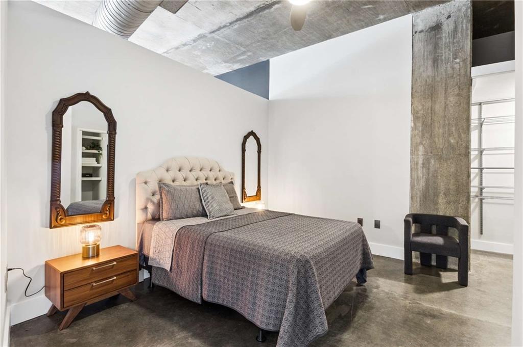 Bedroom with a gray tufted bed, ornate mirrors, polished concrete floor, and exposed ceiling ductwork.