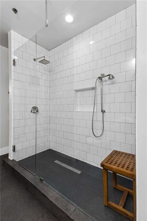 Walk-in shower with white tile walls, two showerheads, dark hexagonal floor tile, and a wooden bench.