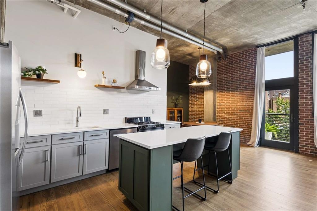 Loft kitchen with gray cabinets, a white island, exposed brick, and tall balcony doors.