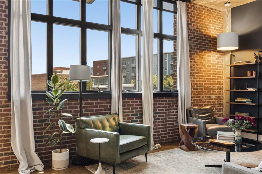 Living room with exposed brick, tall industrial windows, and green leather seating.
