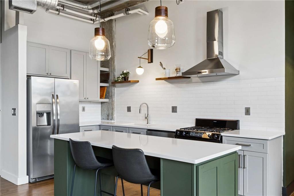 Modern kitchen with a white island, green cabinets, stainless appliances, and two bar stools.
