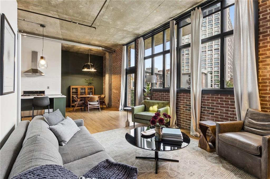 Loft living room with tall industrial windows, exposed brick walls, and an adjoining dining area.