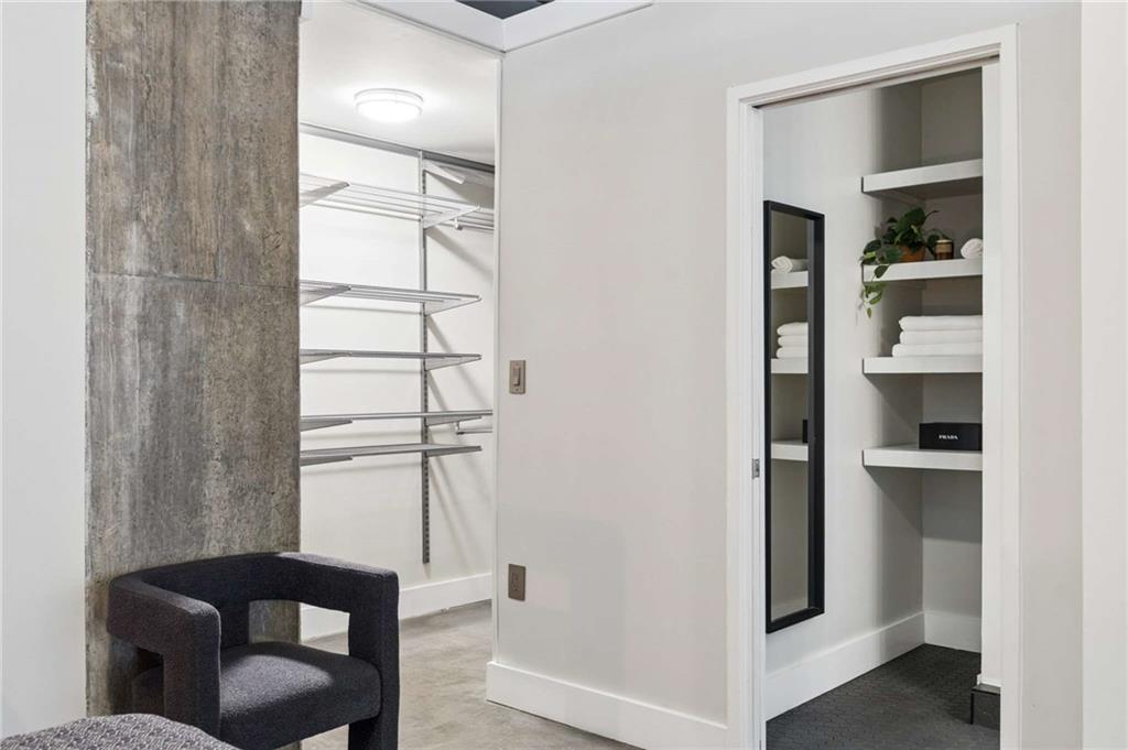 Dressing area with open closet shelving, a concrete column, and a doorway to a bathroom.