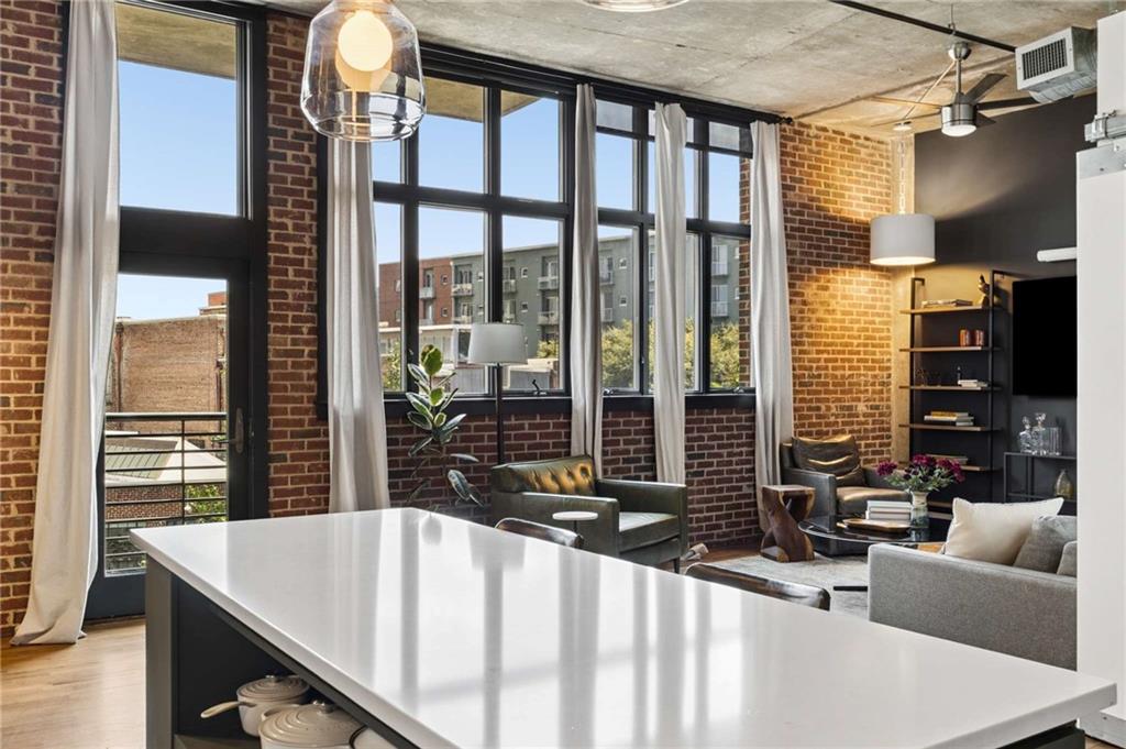 Open-plan loft kitchen and living area with a white island, brick walls, and tall windows.