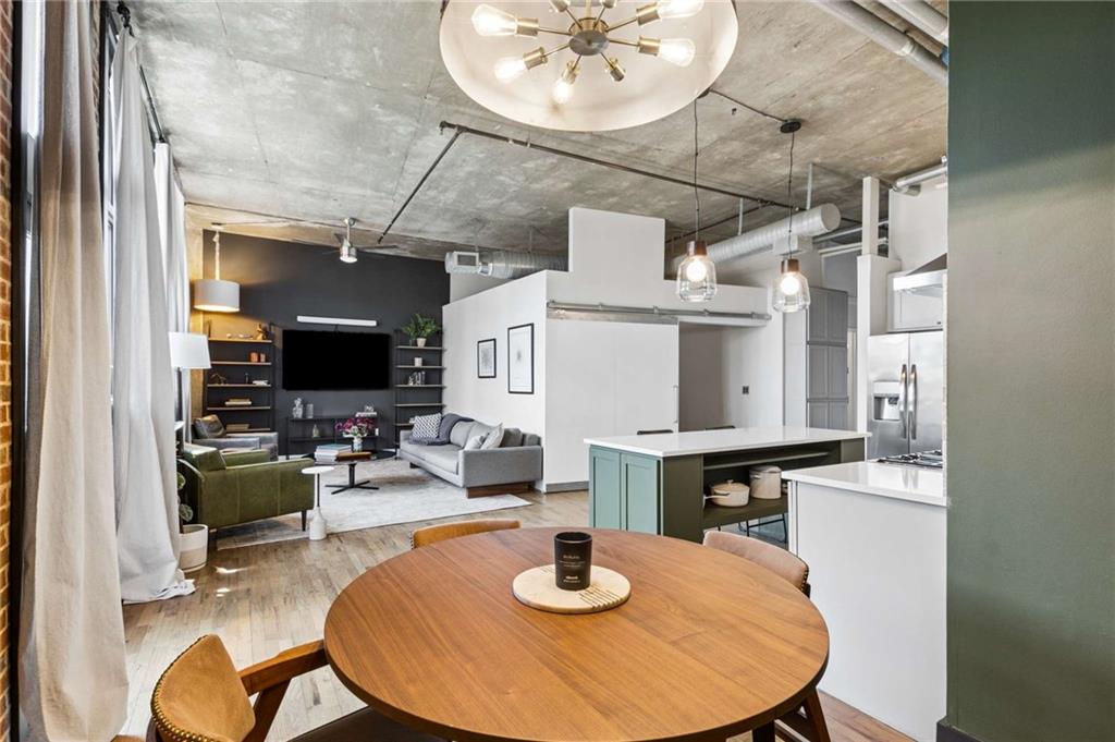 Open-plan condo living area with a round dining table, kitchen island, and exposed concrete ceiling.