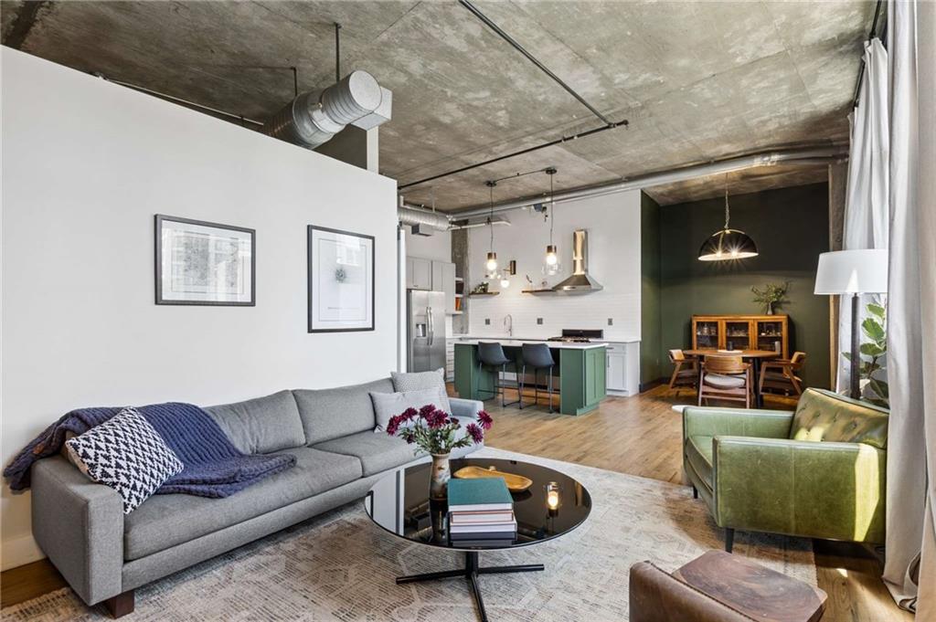 Open-plan living room with gray sofa, green armchair, and green kitchen island beneath a concrete ceiling.