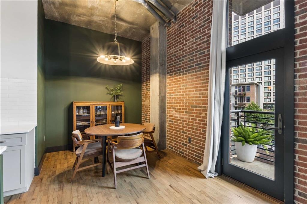 Furnished dining area with a round wooden table, exposed brick walls, and a glass balcony door.