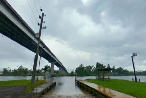 Waterfront launch beneath a large bridge, bordered by grassy banks and wooden edging.