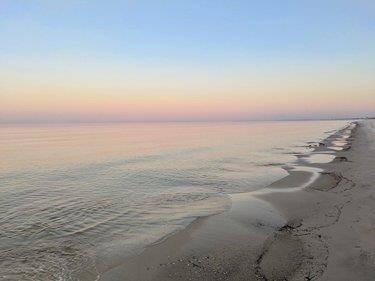 Calm water laps a sandy shoreline beneath a pastel pink and blue dusk sky.