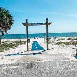 Beach access path crosses sandy dunes toward the ocean beneath a wooden sign.