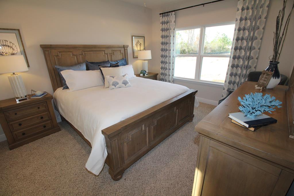 Bedroom with a large wooden bed, white bedding, and a dresser beside a bright window.