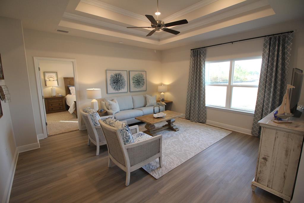 Furnished living room with a blue sofa, patterned armchairs, tray ceiling, and adjoining bedroom doorway.