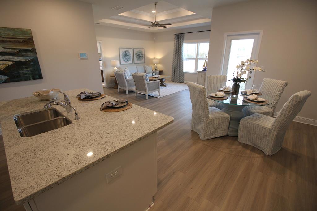 Open-plan kitchen and dining area with a granite peninsula, glass table, and bright windows.