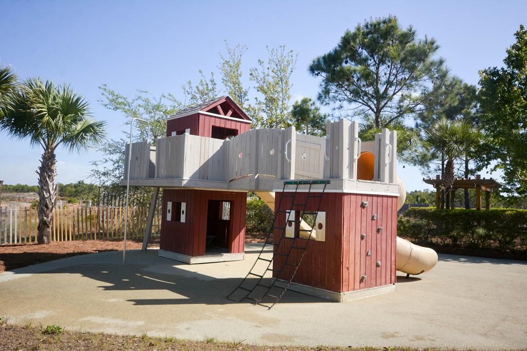 Outdoor playground with a red-and-gray play structure, climbing wall, ladders, and tube slide.