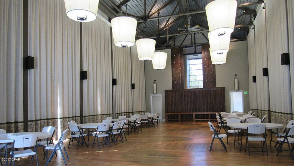 Large hall with folding chairs and tables, polished wood floor, and a raised platform.