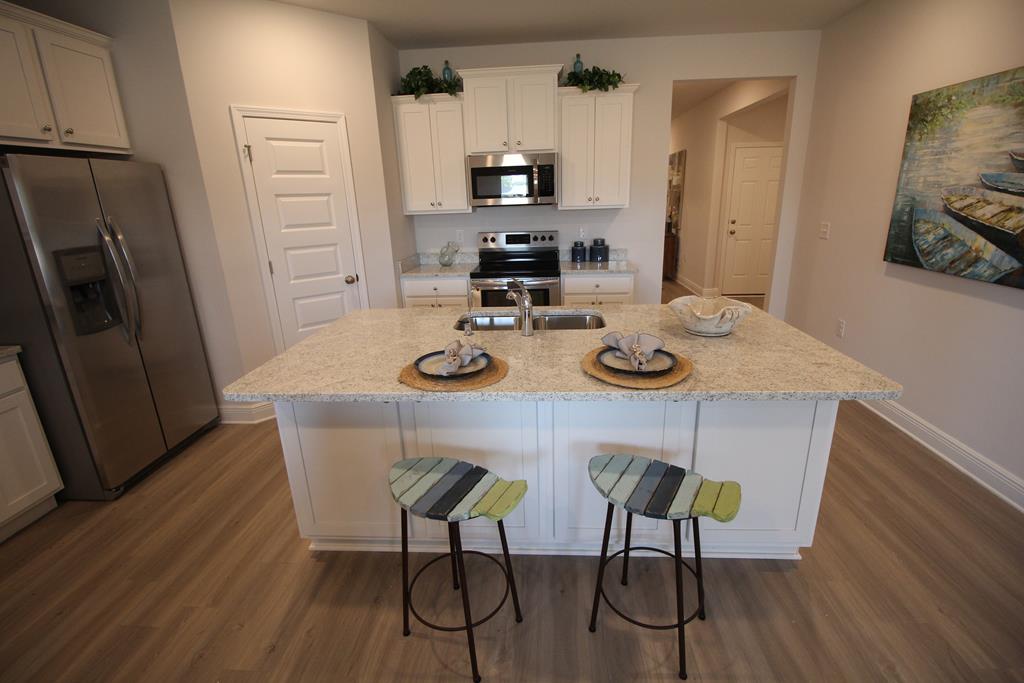 Staged kitchen with white cabinets, stainless steel appliances, and a large island with two stools.