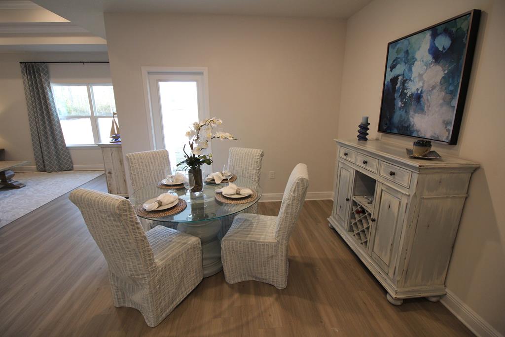 Dining room with a glass table, woven chairs, and a white sideboard beneath blue abstract art.