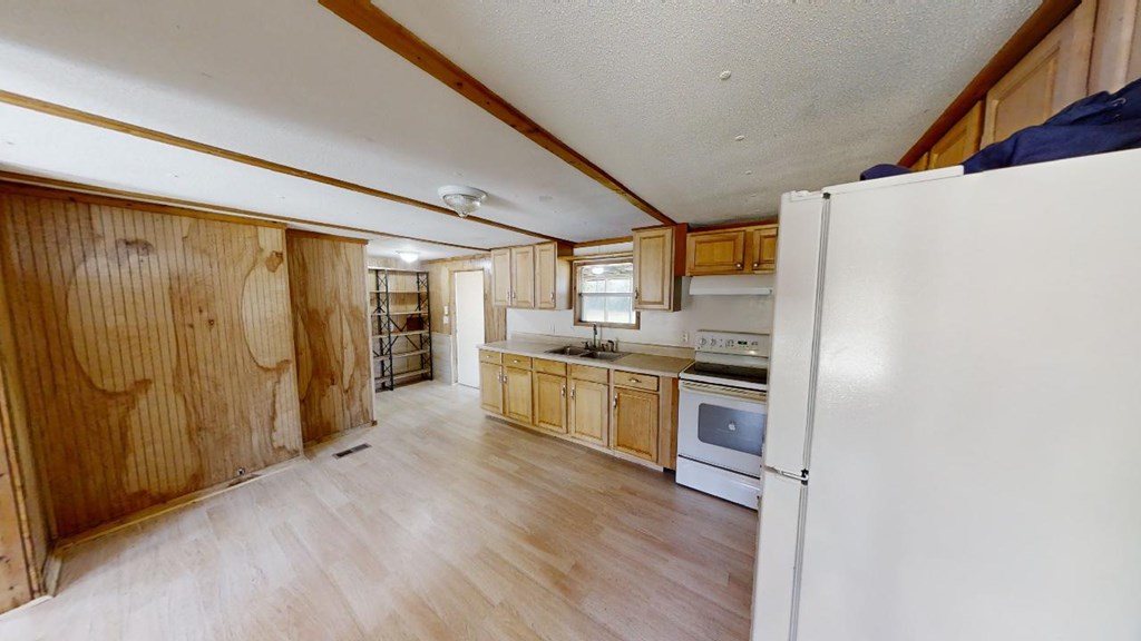 Kitchen with light wood cabinets, white appliances, and wood-paneled walls.
