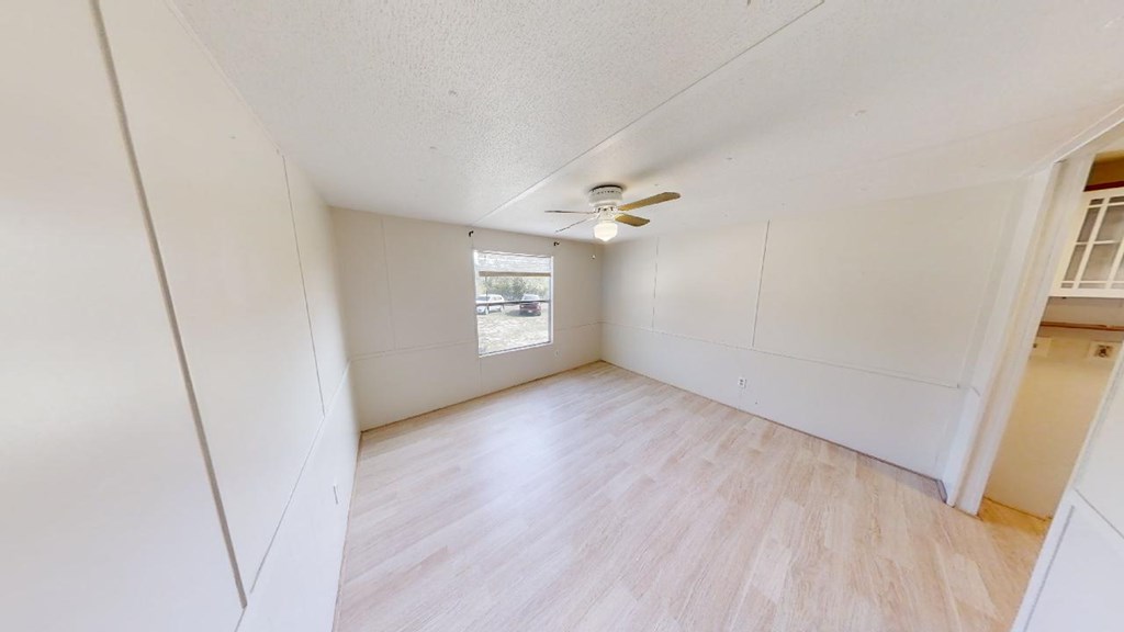 Empty room with pale flooring, a ceiling fan, and a window overlooking the yard.