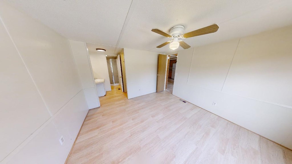 Empty room with white paneled walls, pale flooring, and a ceiling fan.