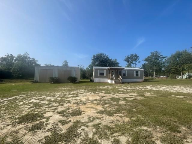 Manufactured home with a front porch and detached metal shed on a patchy sandy lawn.