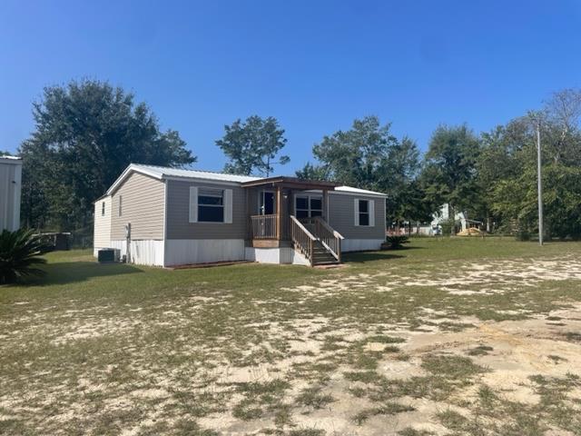 Manufactured home with a covered front porch and sandy, patchy lawn.