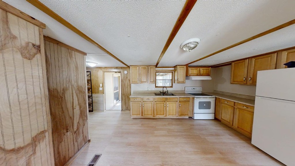 Kitchen with light wood cabinets, white appliances, and wood-paneled walls.