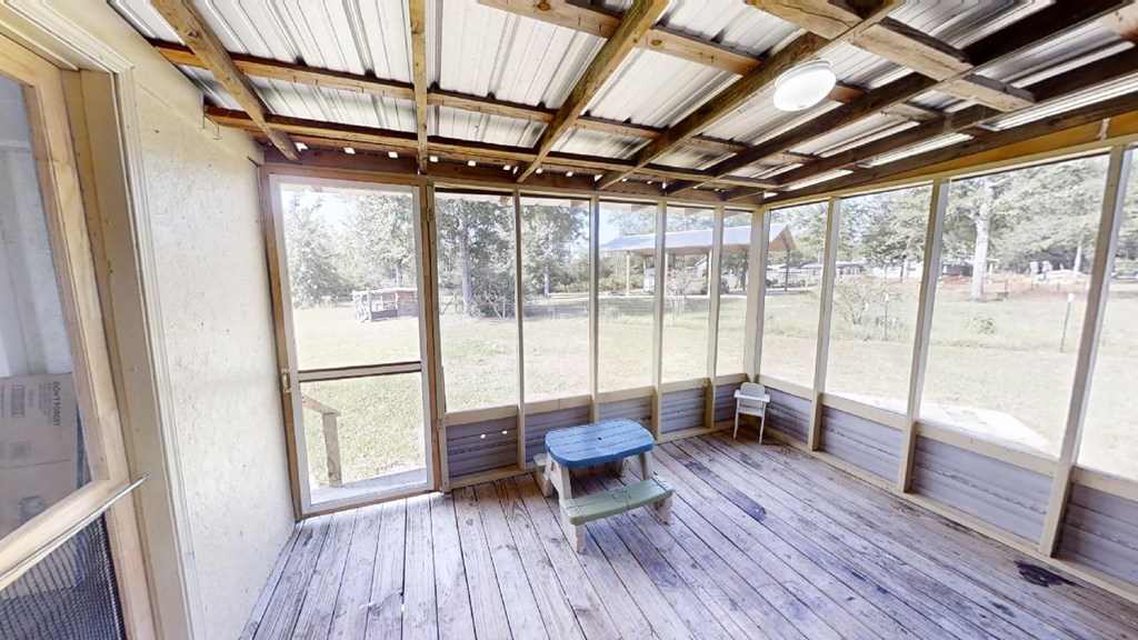 Screened-in porch with exposed ceiling beams, weathered plank flooring, and a small blue table with benches.