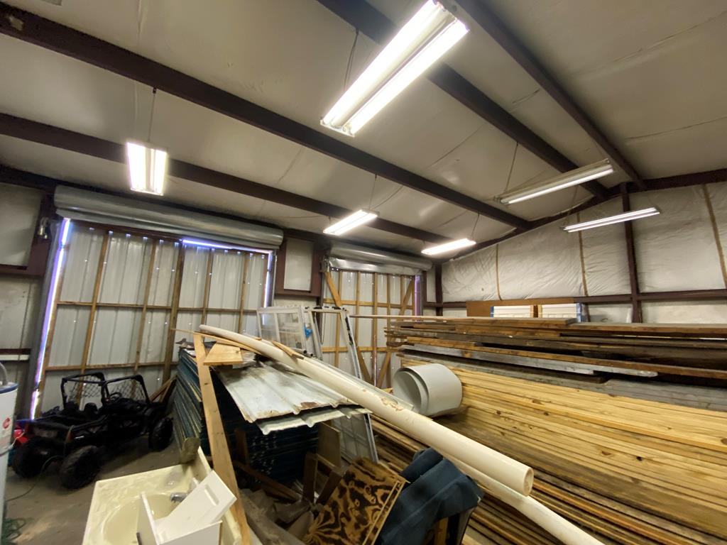 Workshop interior with stacked lumber, building materials, and fluorescent lights.