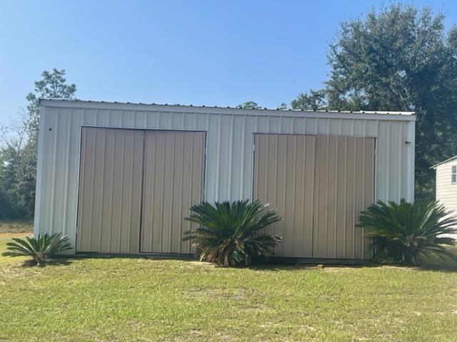 Detached metal outbuilding with two roll-up doors and small palms along the front.