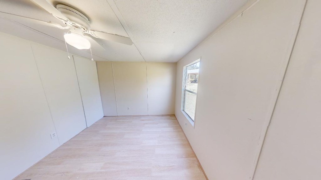 Empty room with light wood-look flooring, a ceiling fan, and one window.