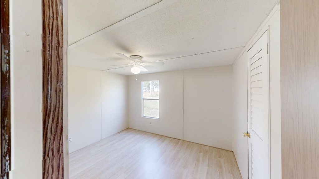 Empty bedroom with light wood-look flooring, a ceiling fan, and a louvered closet door.