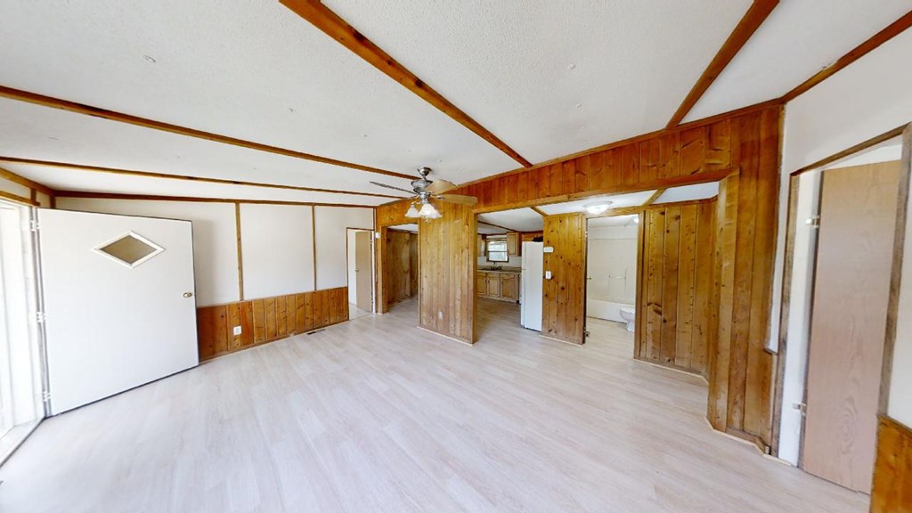 Vacant living room with wood-paneled walls, exposed ceiling beams, and light flooring.
