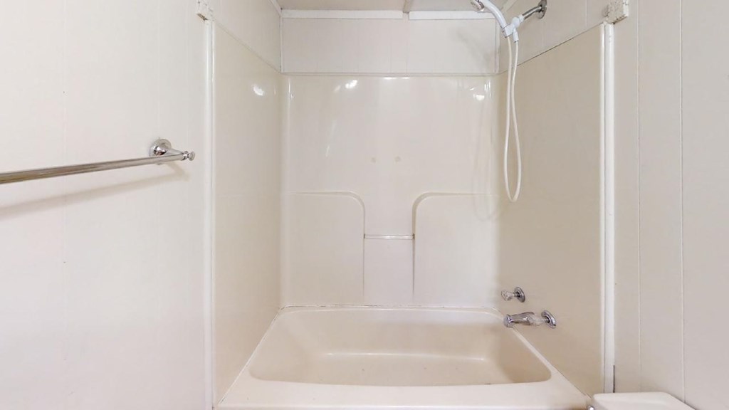 White bathtub and shower with handheld showerhead and chrome fixtures.