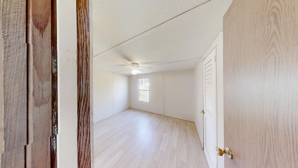 Empty bedroom with light wood-look flooring, a ceiling fan, and a louvered closet door.