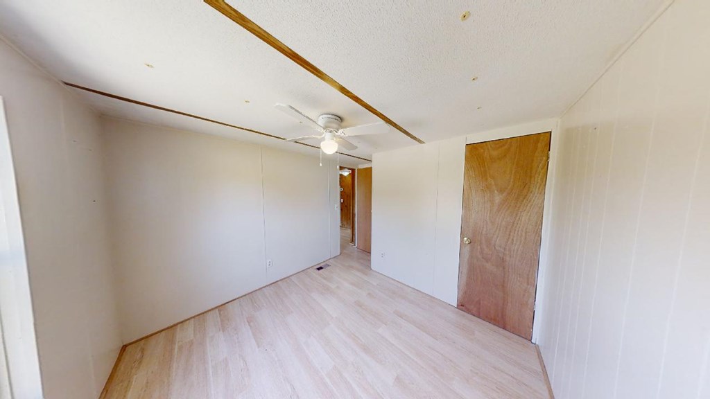 Empty room with pale flooring, white walls, ceiling fan, and wooden doors.